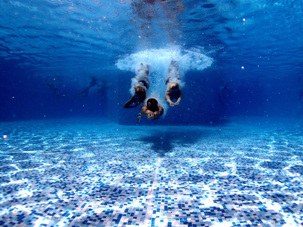 three people diving into water pool